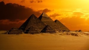Orange hue over the great pyramids of Egypt. Semi Cloudy sky above and reddish hue desert sand below